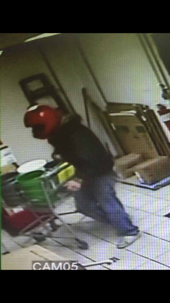 Robber wearing red helmet pushing a cart, shown on security camera image