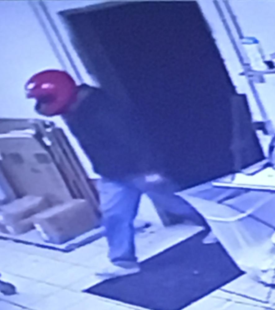 Robber walking through doorway wearing red motorcycle helmet, blue jeans and black sweatshirt