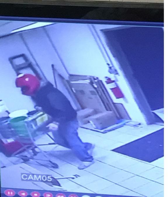 Security camera screenshot of robber with red motorcycle helmet, blue jeans, white shoes, and black sweatshirt
