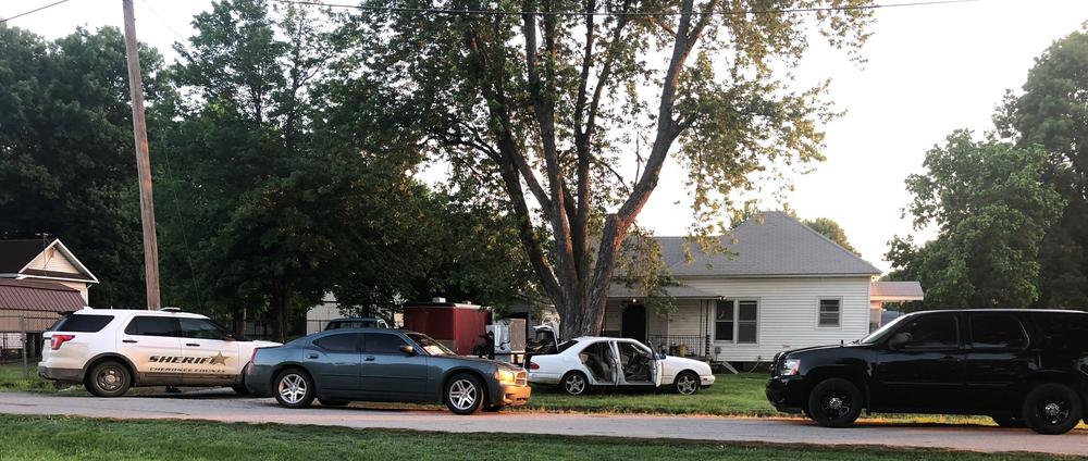 police vehicles outside residence, with white vehicle in yard with all doors and trunk open