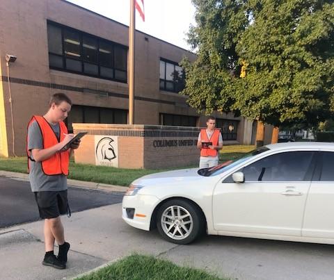 Student in orange vest writing on clipboard