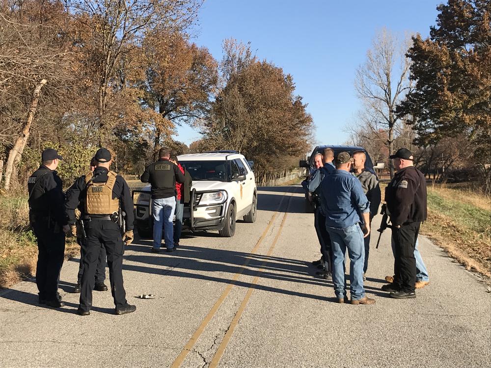 Officers and bystanders standing in the road with one police vehicle