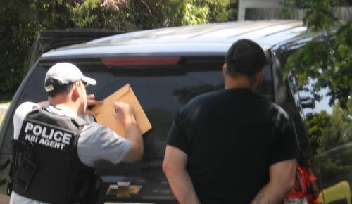 Officer writing on manila envelope on back of police vehicle